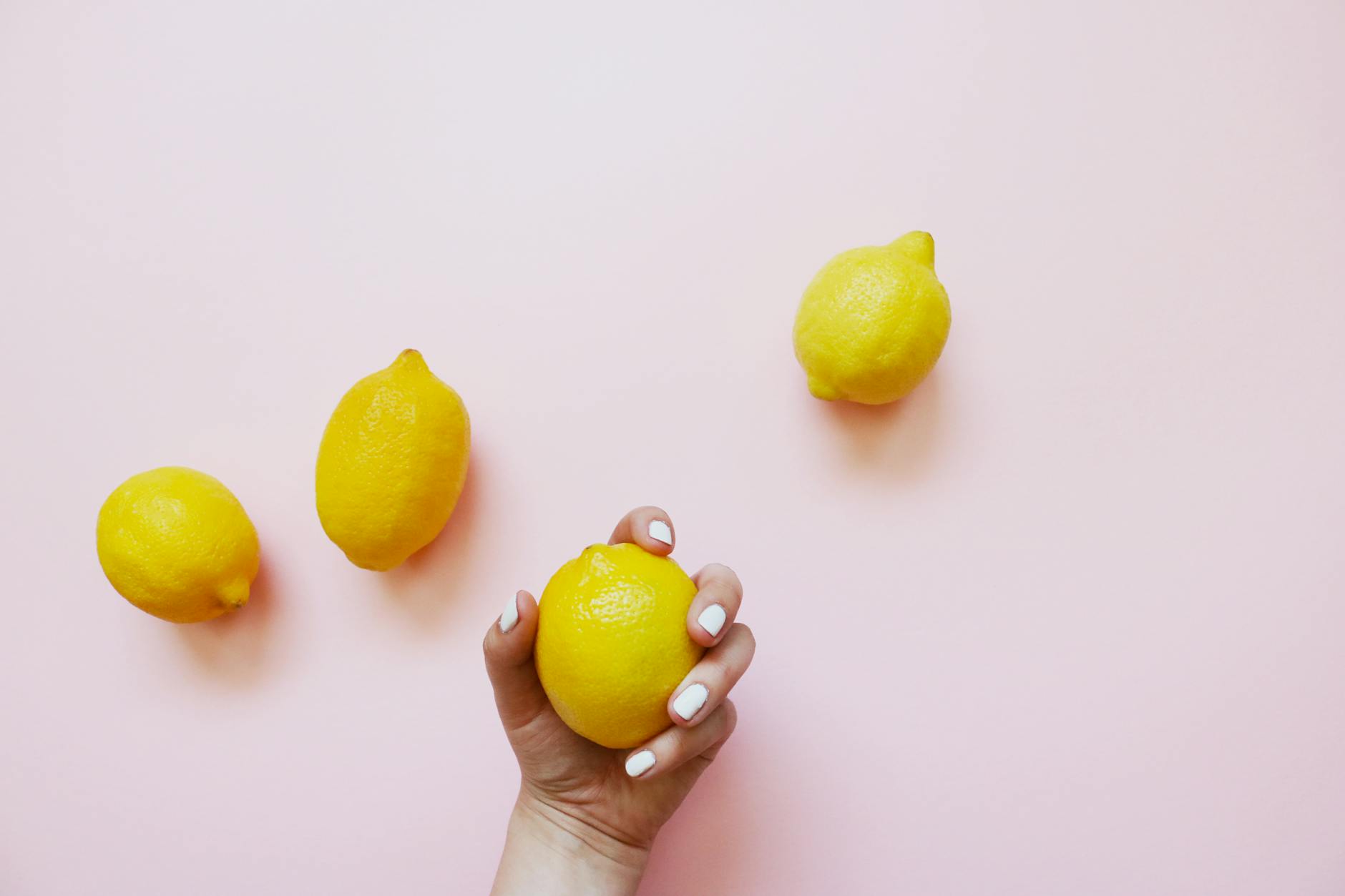 A hand holding a bright lemon on a soft pink background, symbolizing the natural, responsive pleasure of lemon clitoral vibrators