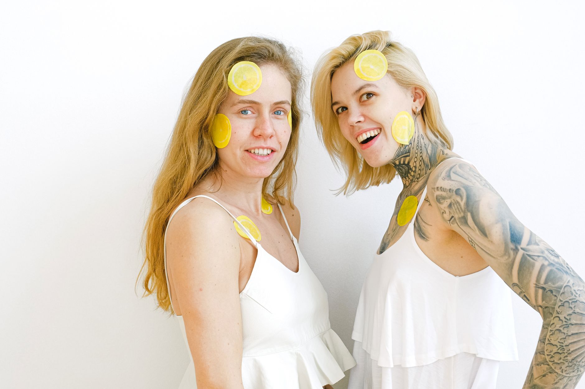 Two smiling women enjoying time together with lemon slices on their faces, symbolizing freshness and joy