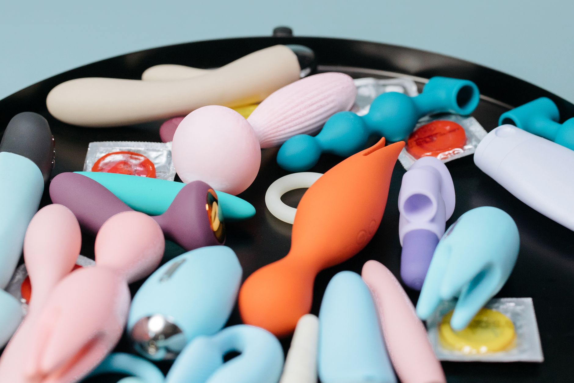 A vibrant collection of various sex toys on a black tray, featuring diverse shapes and colors including a yellow lemon vibrator.