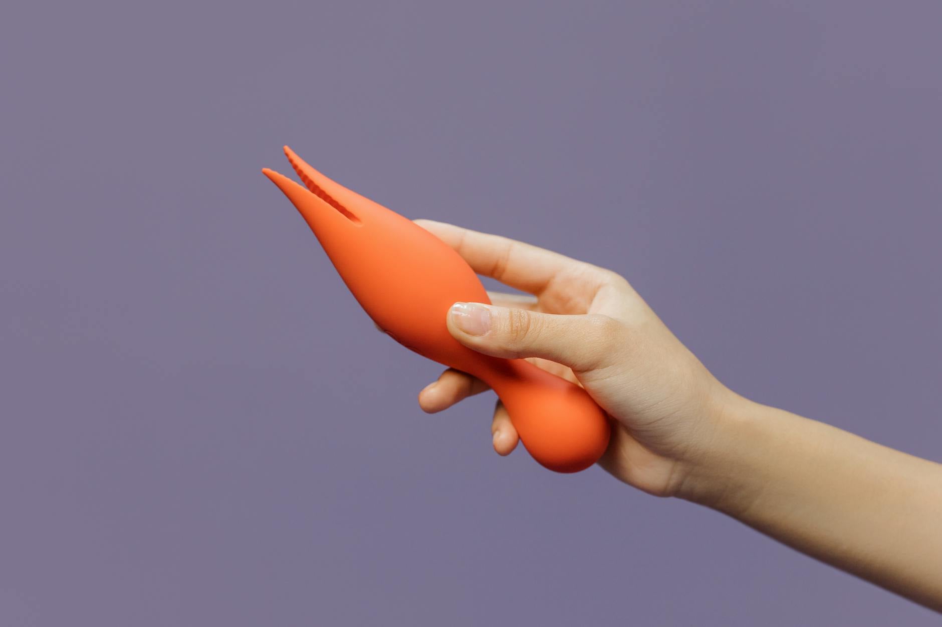 A hand holding a lemon-colored clitoral vibrator against a minimalistic purple backdrop