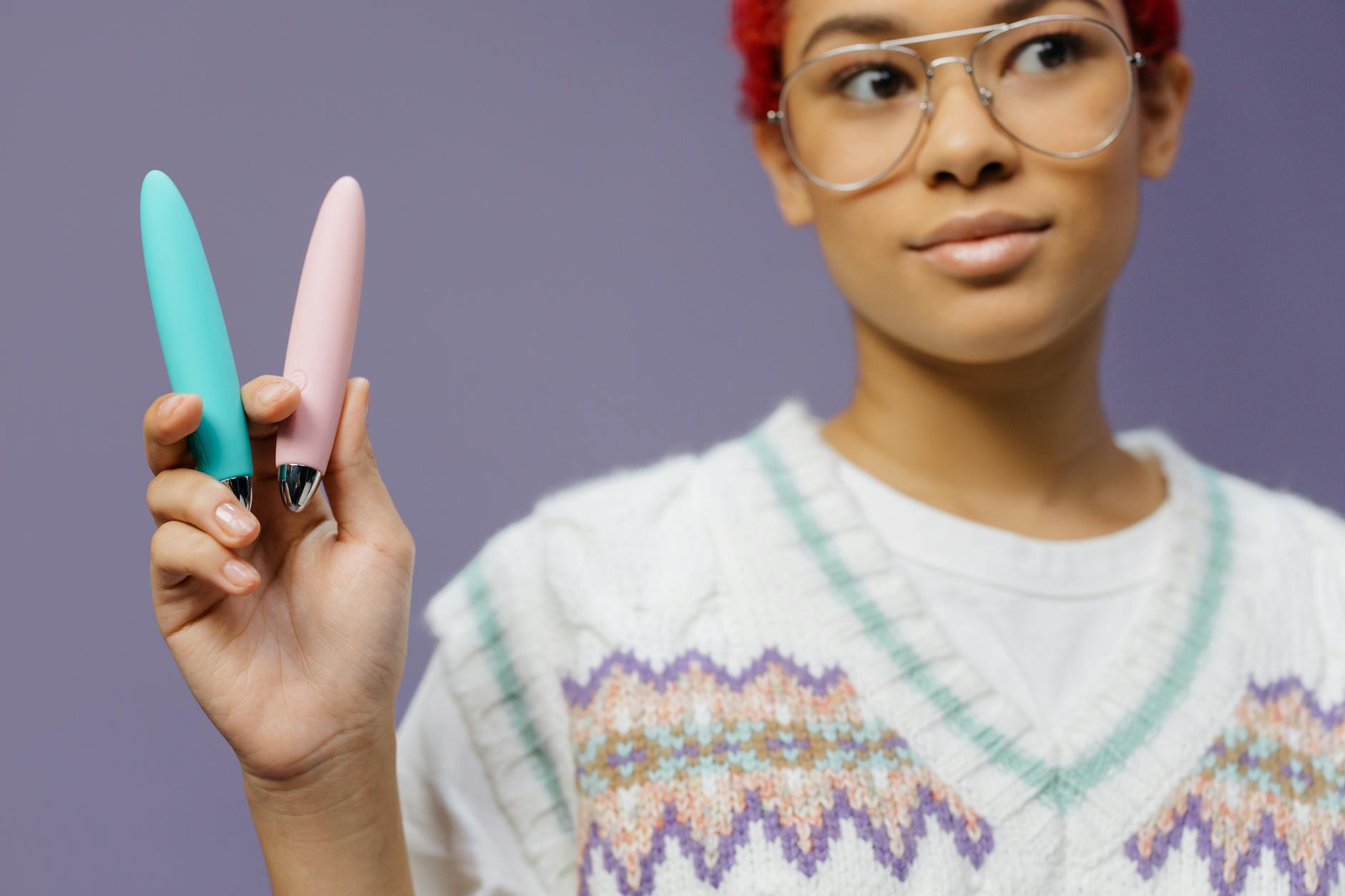 A person holding two colorful vibrators against a purple background, representing modern pleasure tools.