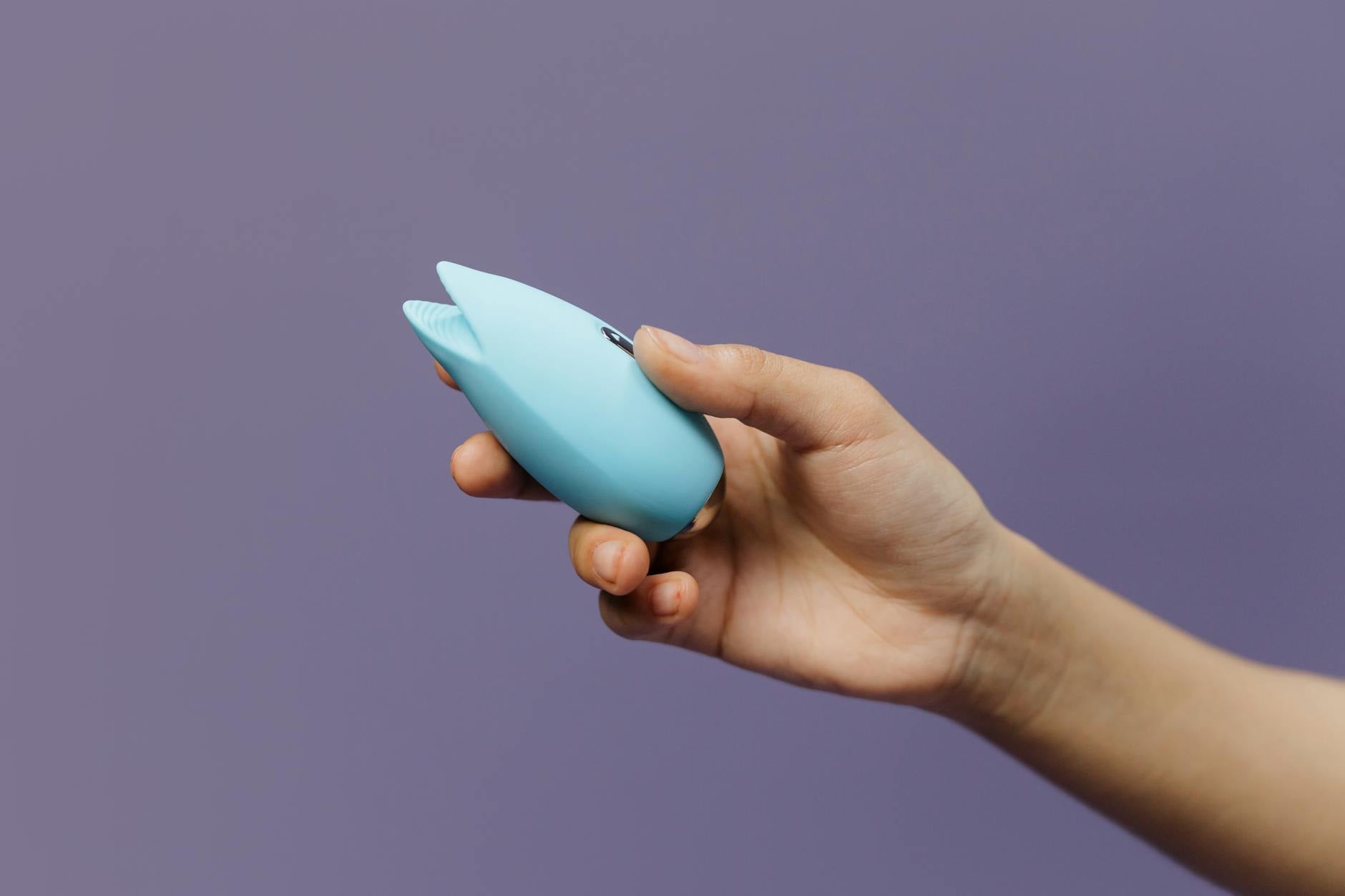 A hand holding a silicone sex toy against a purple background, representing self-pleasure and sexual wellness