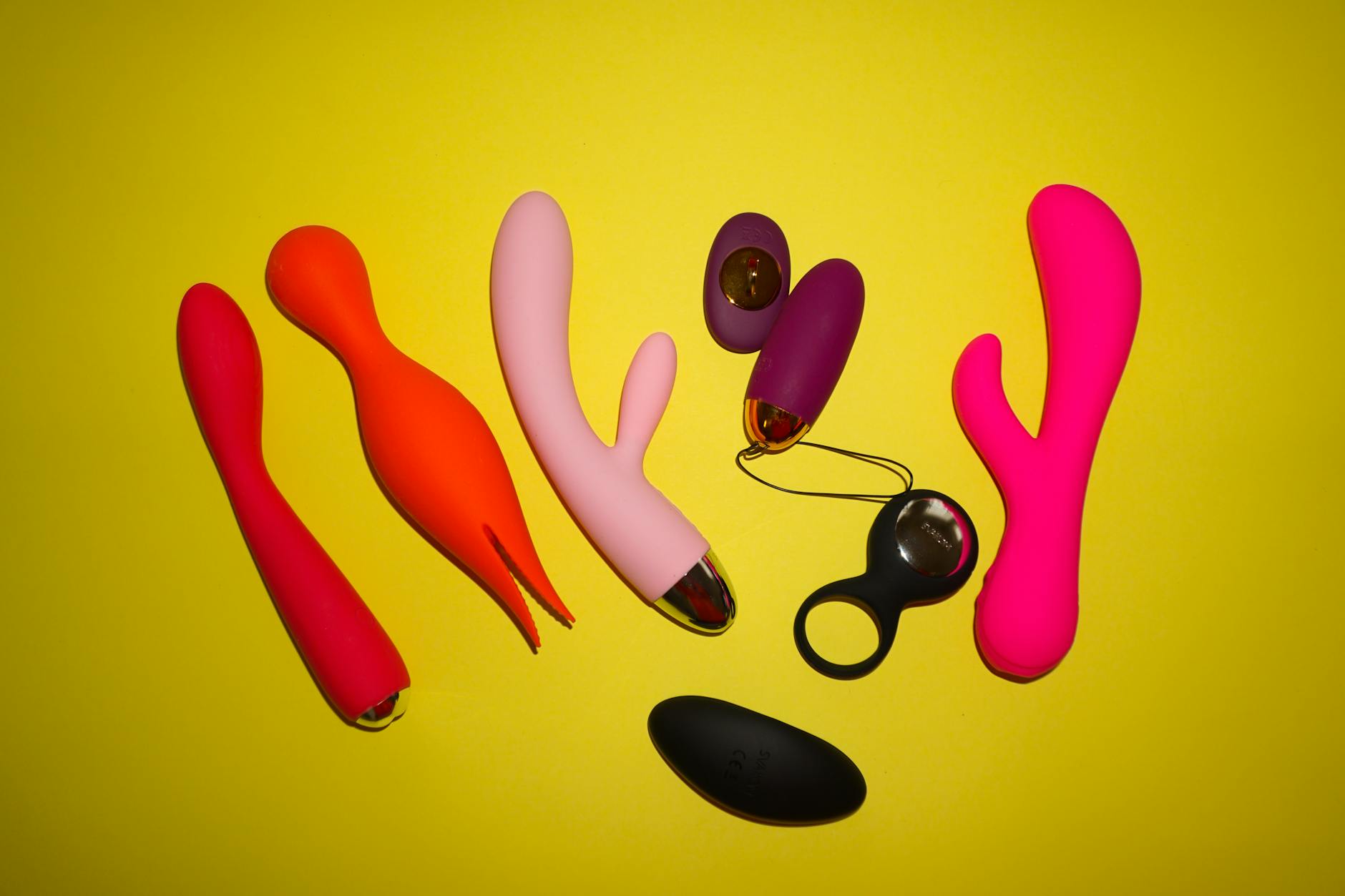 Studio setup showcasing colorful clitoral vibrators and sexual wellness toys on a bright yellow background